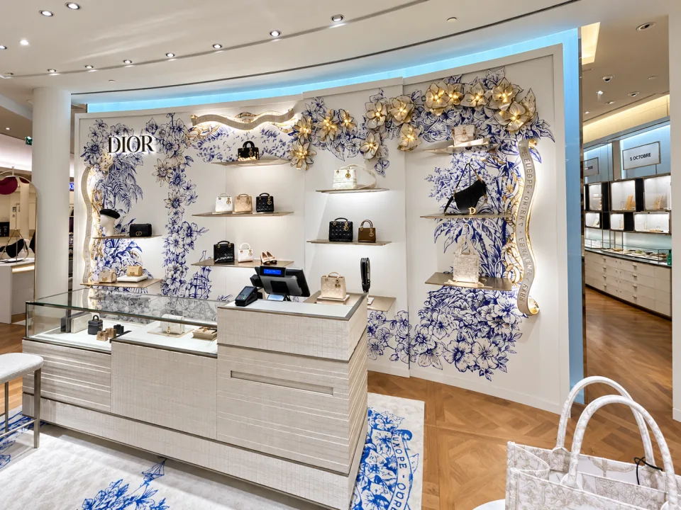 Décoration murale boutique Dior : corner habillé d'un décor botanique bleu sur mur blanc, grandes fleurs dorées en relief, étagères de sacs et comptoir