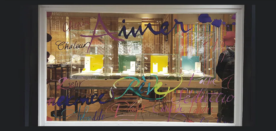 Vitrine Arthus-Bertrand habillée d'un lettrage manuscrit multicolore en adhésif, bijoux exposés visibles derrière le vitrage