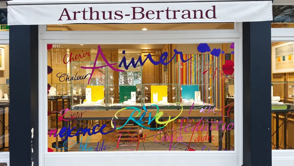 Vitrine de Noël Arthus-Bertrand : mots manuscrits colorés en vitrophanie (« Aimer », « Rêve », « Chérir ») sur le vitrage, bijoux exposés visibles derrière