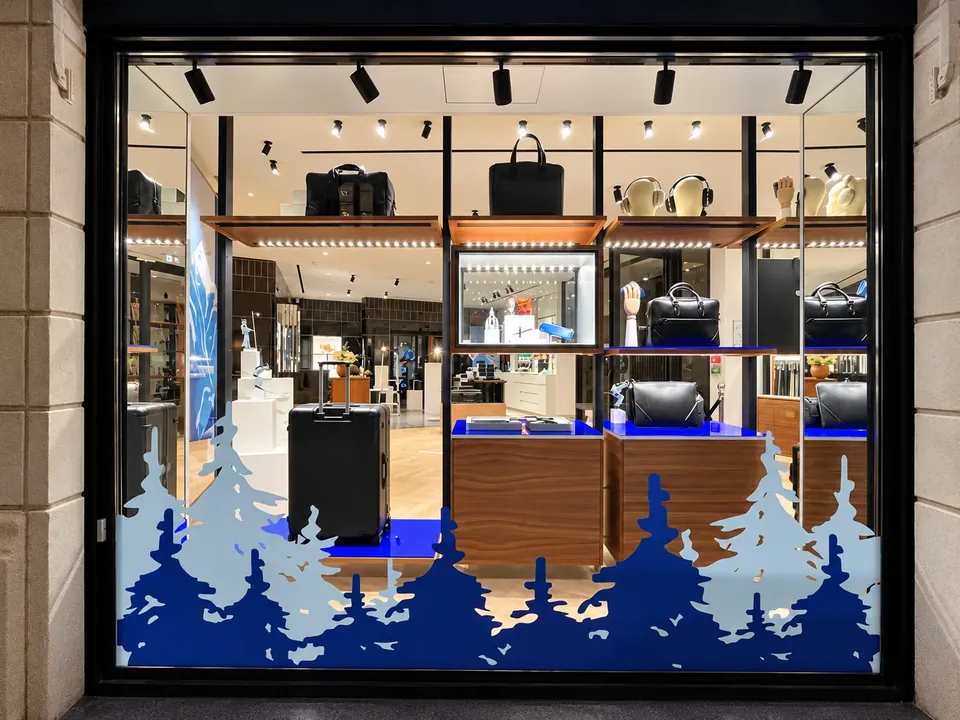 Vitrine de Noël Montblanc de nuit : forêt de sapins bleus en vitrophanie en partie basse, boutique éclairée visible au-dessus